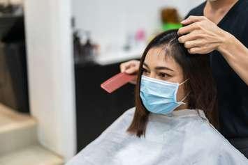 A woman wears a facemask while getting a haircut. (© Can Stock Photo / geargodz)