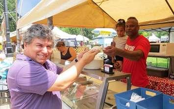 Sunfest Artistic Director Alfredo Caxaj grabs lunch from Triniman Kitchen Owner Joseph Alexander and his granddaughter 2-year-old Gabriella, July , 2018. Alexander is one of 65 food vendors at Sunfest. (Photo by Miranda Chant, Blackburn News)