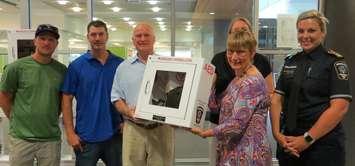 John Sweitzer, Chris Lynch, and Doug Cairns hand over a donated AED to the London Public Library's Nancy Collister and Kim Travers (back) and Middlesex London Paramedic Service's Miranda Bothwell, August 1, 2018. (Photo by Miranda Chant, Blackburn News) 